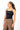 A woman wearing a black square-neck tank top with thin straps and a small white script logo on the chest, paired with brown pants, photographed against a plain white studio background.