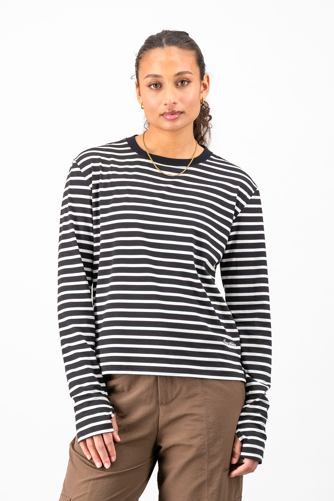 A woman modeling a black and white horizontally striped long-sleeve knit top with a crew neck, paired with brown pants, against a plain white studio background.