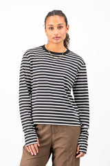 A woman modeling a black and white horizontally striped long-sleeve knit top with a crew neck, paired with brown pants, against a plain white studio background.